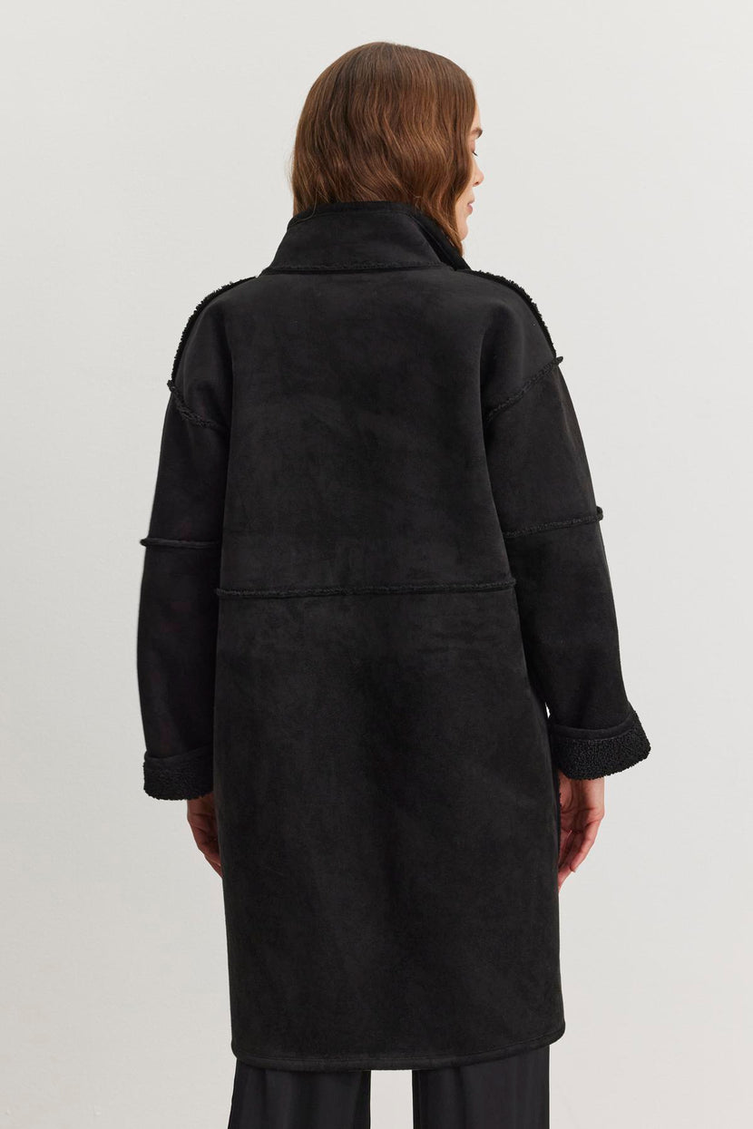 A person wearing a long black CARA LUXE SHERPA REVERSIBLE JACKET by Velvet by Graham & Spencer, shown from the back against a plain background, its subtle faux suede texture adding a touch of elegance.