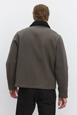 A person with short hair, wearing the Velvet by Graham & Spencer CASH JACKET featuring a dark full-zip design with a black faux sherpa collar and paired with black pants, is seen from the back against a plain background.