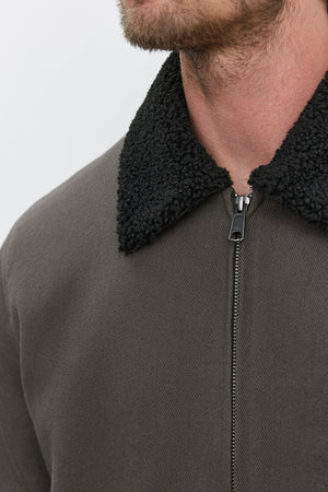 Close-up of a person wearing the Velvet by Graham & Spencer CASH JACKET, which features a dark green full-zip design with a textured black faux sherpa collar. The front is partially zipped, revealing the lower part of the face.