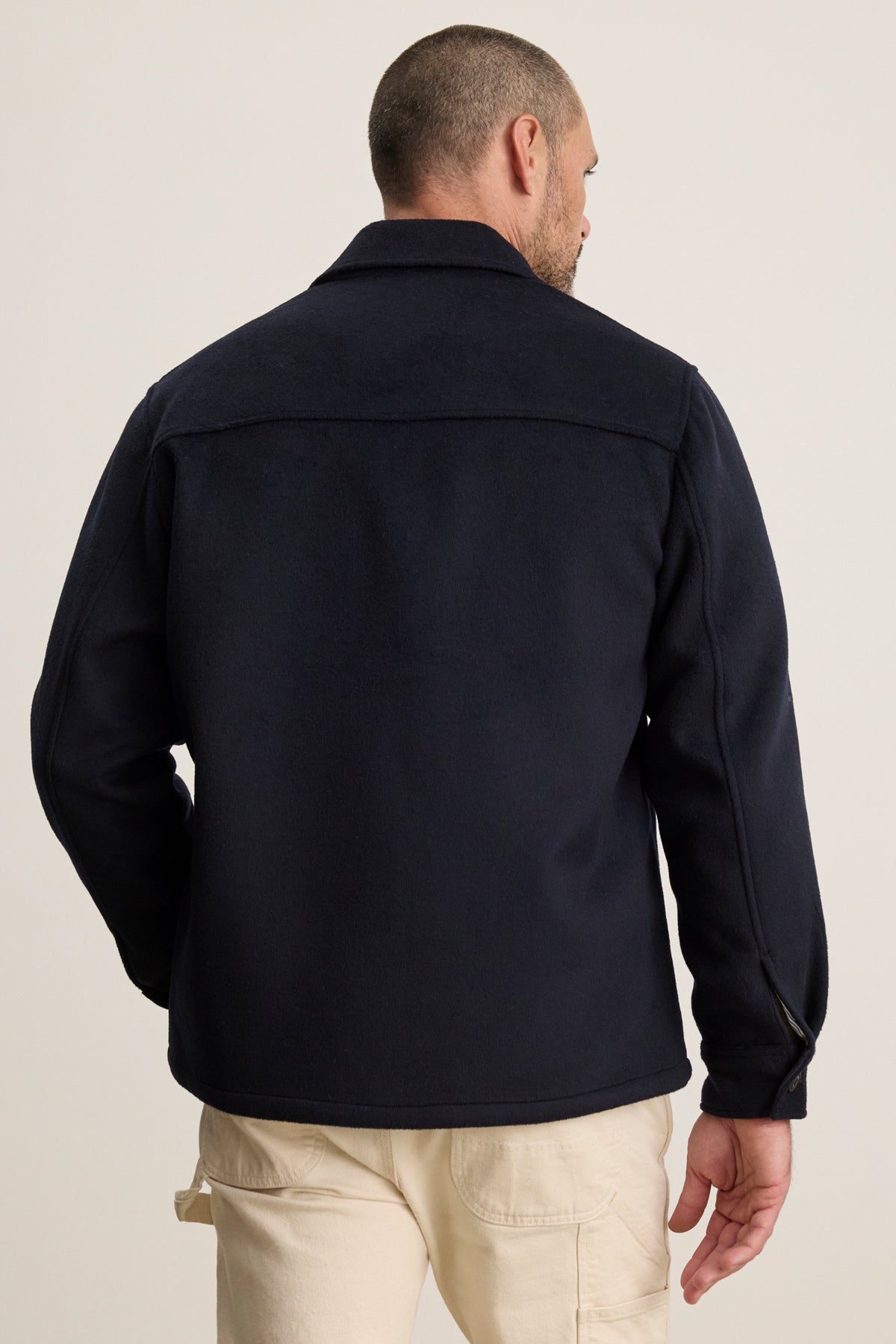 A man wearing the EMERSON CHORE JACKET by Velvet by Graham & Spencer and light-colored pants stands with his back to the camera against a plain background.