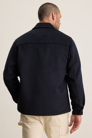 A man wearing the EMERSON CHORE JACKET by Velvet by Graham & Spencer and light-colored pants stands with his back to the camera against a plain background.