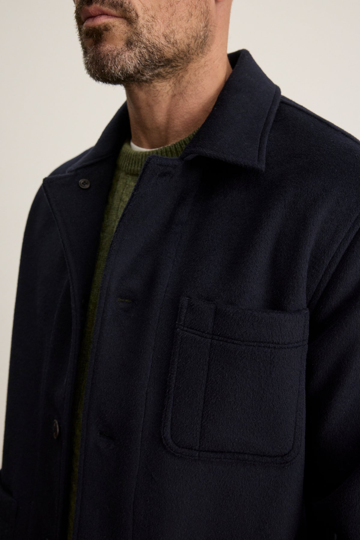 A man wears the Velvet by Graham & Spencer EMERSON CHORE JACKET, a dark navy wool blend, over a green knit sweater, shown from shoulders to mid-chest with emphasis on the jacket’s front pocket.