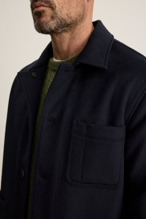A man wears the Velvet by Graham & Spencer EMERSON CHORE JACKET, a dark navy wool blend, over a green knit sweater, shown from shoulders to mid-chest with emphasis on the jacket’s front pocket.