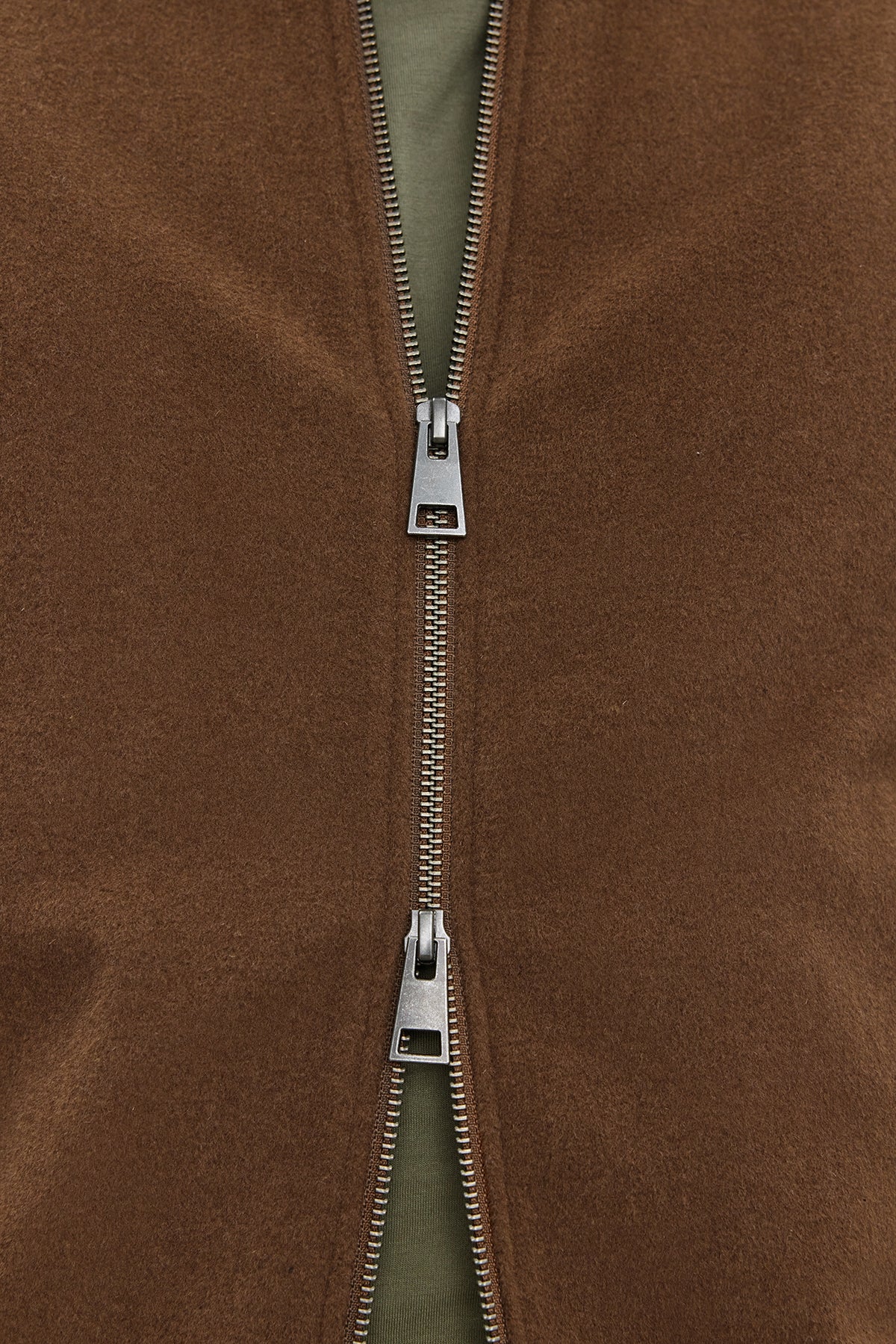   Close-up of a partially unzipped FRAZIER BOMBER JACKET by Velvet by Graham & Spencer, revealing a green inner layer. The silver-colored zipper boasts a prominent mechanism, while the wool blend ensures lasting warmth. 