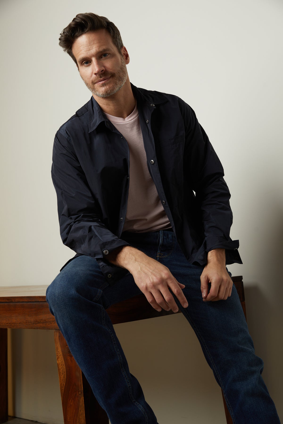   A man sitting on a wooden bench wearing Velvet by Graham & Spencer jeans and a shirt. 