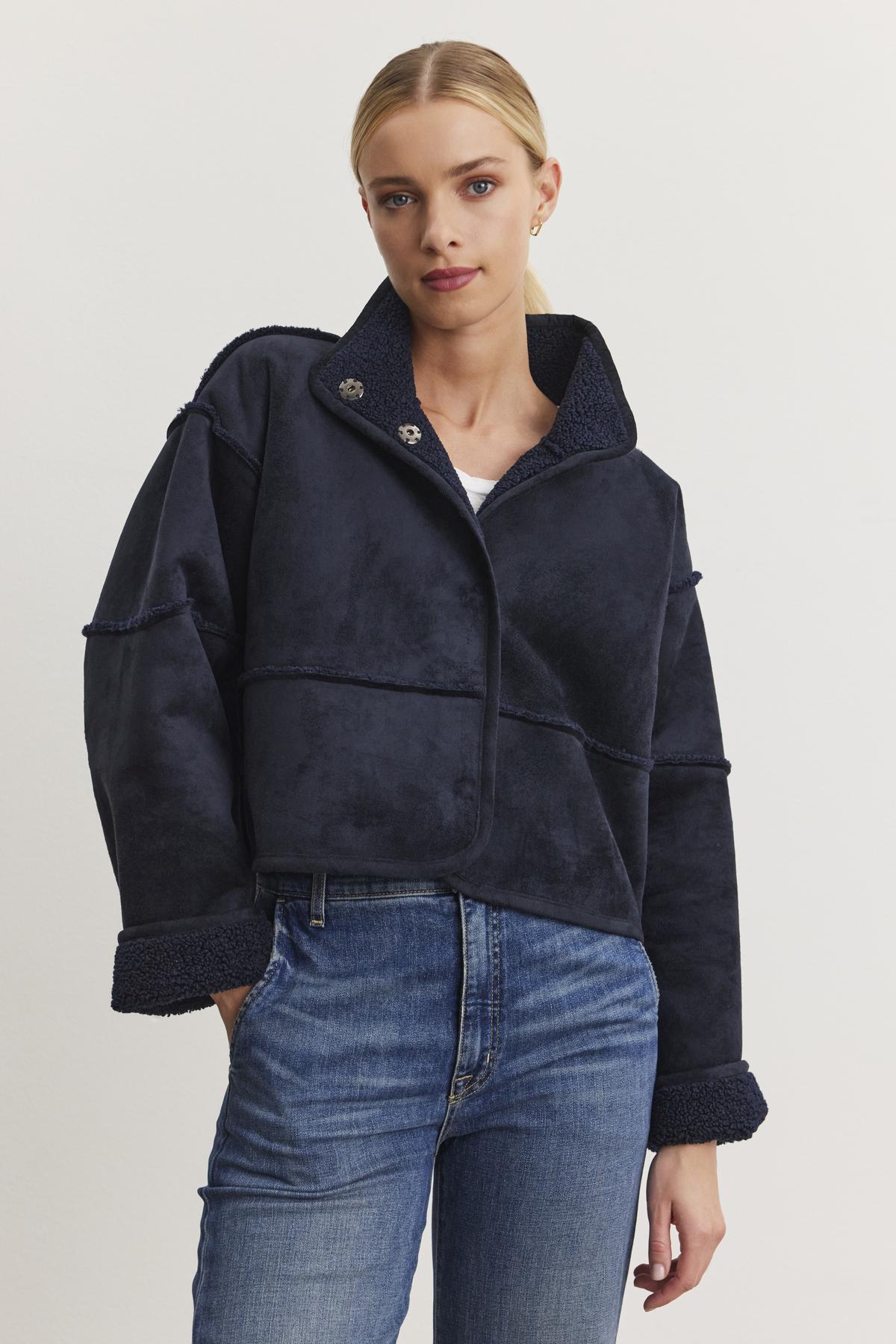 Dressed in a dark blue KELLY LUXE SHERPA REVERSIBLE JACKET from Velvet by Graham & Spencer over a white top and blue jeans, the person stands against a plain background, radiating effortless style.-38219209998529