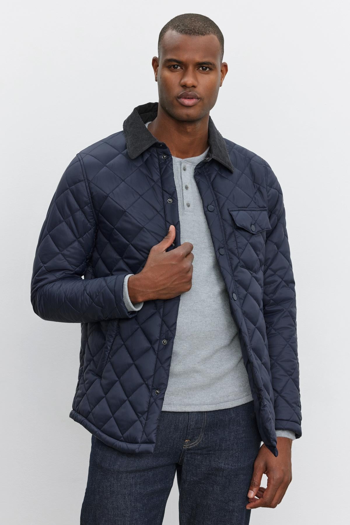 A person in a LOU JACKET by Velvet by Graham & Spencer, featuring a quilted puffer design with a corduroy collar, is wearing a light grey henley shirt and blue jeans.-37888570392769