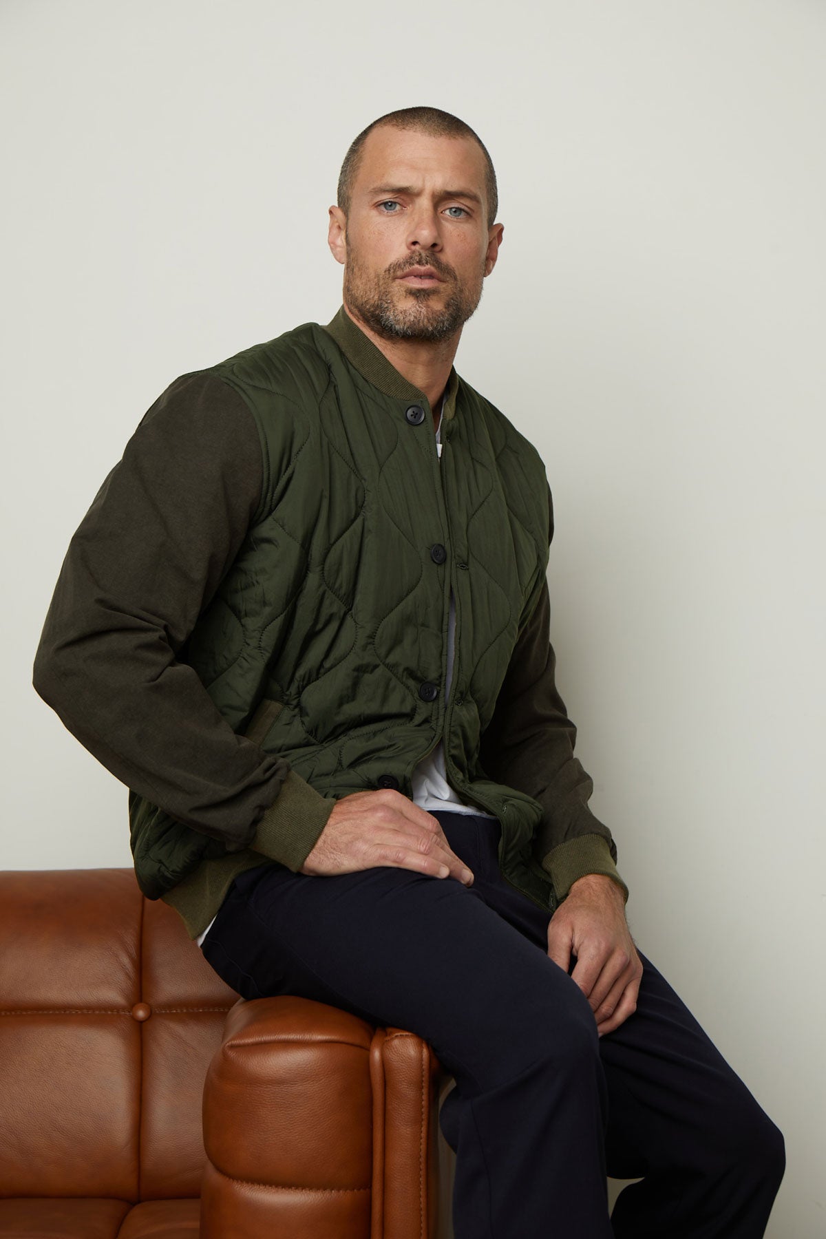 A man sitting on a brown leather couch wearing a Velvet by Graham & Spencer MAISON quilted jacket exudes style and functionality.-35605815197889