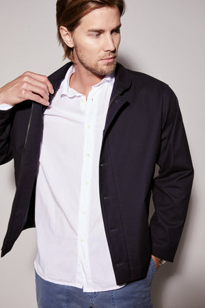 A man is posing in a blue jacket and white Velvet by Graham & Spencer BROOKS BUTTON-UP SHIRT.