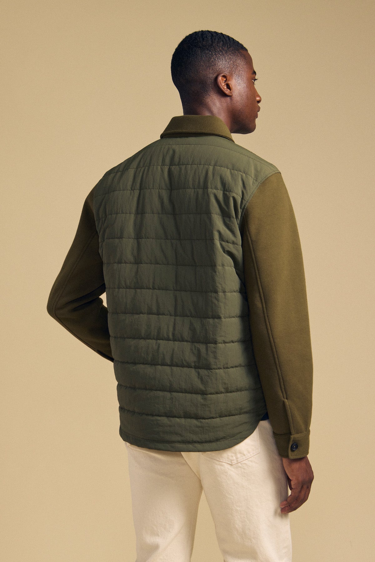 Back view of a man wearing an olive green RYKER QUILTED JACKET with solid sleeves, ideal for transitional weather.