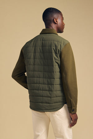 Back view of a man wearing an olive green RYKER QUILTED JACKET with solid sleeves, ideal for transitional weather.