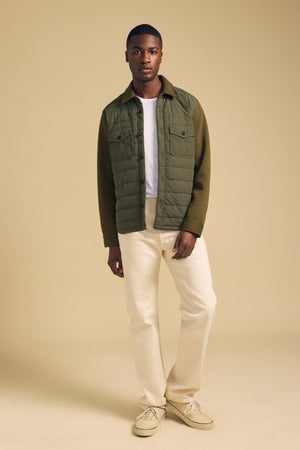 A man wearing an olive green RYKER QUILTED JACKET by Velvet by Graham & Spencer over a white t-shirt, off-white trousers, and tan sneakers.