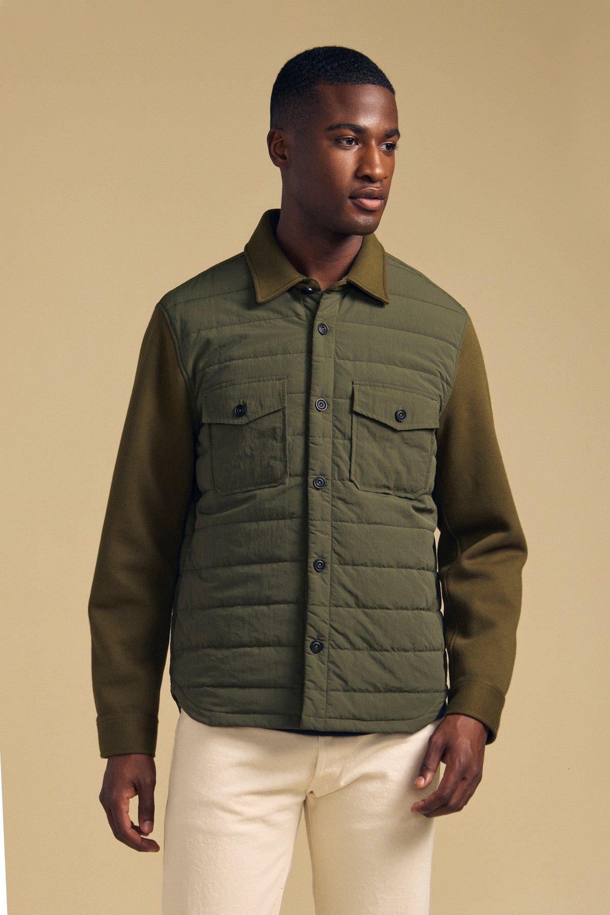 A man wears the olive green RYKER QUILTED JACKET, featuring a button-down front, chest pockets, and a quilted front panel, perfect for transitional weather.