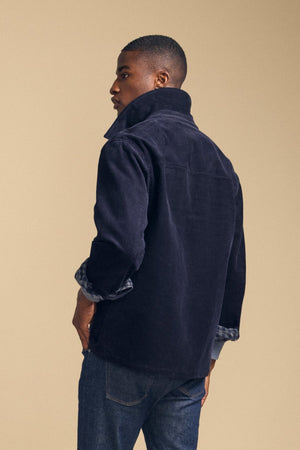 A person stands with their back to the camera, wearing the SEGAL CORDUROY JACKET by Velvet by Graham & Spencer with the collar up and blue jeans against a beige background.