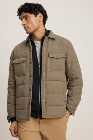 A man wears the SUMMIT JACKET by Velvet by Graham & Spencer—a taupe quilted cotton piece with snap buttons—over a dark zip-up top and tan pants, standing against a plain light background.