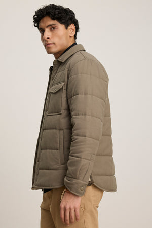A man in the SUMMIT JACKET by Velvet by Graham & Spencer—a light brown quilted cotton jacket with snap buttons and multiple pockets—paired with tan pants, stands sideways against a neutral background.