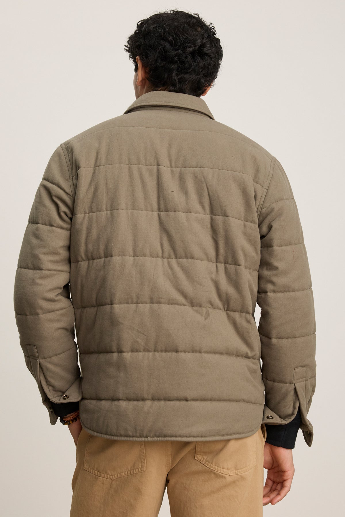 A person is seen from behind wearing the SUMMIT JACKET by Velvet by Graham & Spencer—a khaki quilted cotton jacket with multiple pockets—paired with light brown pants, set against a plain background.-39841114128577