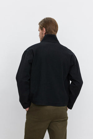 A person with light brown hair is seen from behind, wearing the WILBUR JACKET by Velvet by Graham & Spencer and olive green twill pants with a button front, standing against a plain white background.