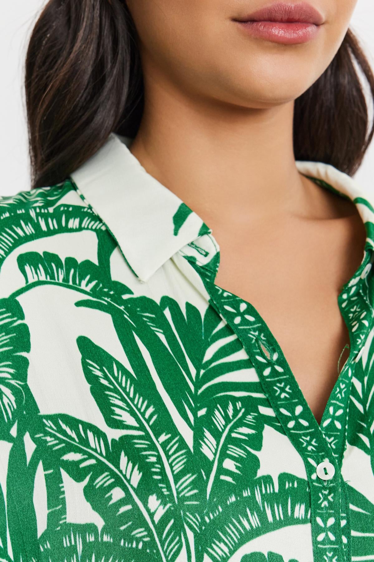   Close-up of a woman wearing a green and white palm print AYLA BUTTON-UP SHIRT by Velvet by Graham & Spencer, focusing on the collar and top buttons. 