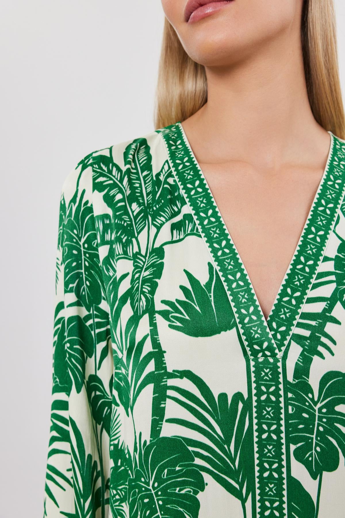   Close-up of a woman wearing a green and white palm print Emella dress by Velvet by Graham & Spencer with a v-neckline. 