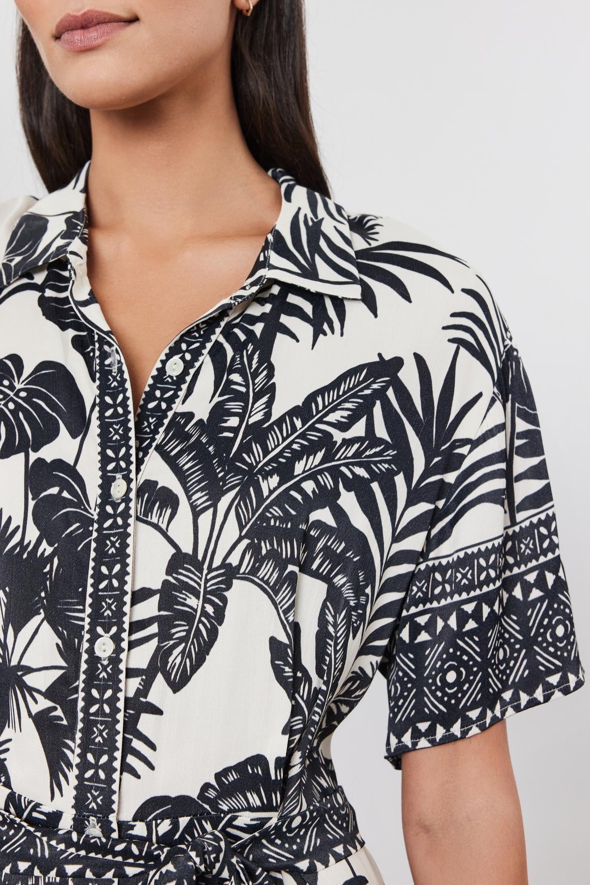   Close-up of a woman wearing a black and white palm print FREYA DRESS by Velvet by Graham & Spencer with a zipper front. 