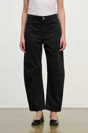 A person wears a white t-shirt, Velvet by Graham & Spencer's BRYLIE SANDED TWILL UTILITY PANT in black with patch pockets, and black flat shoes, standing against a plain background.