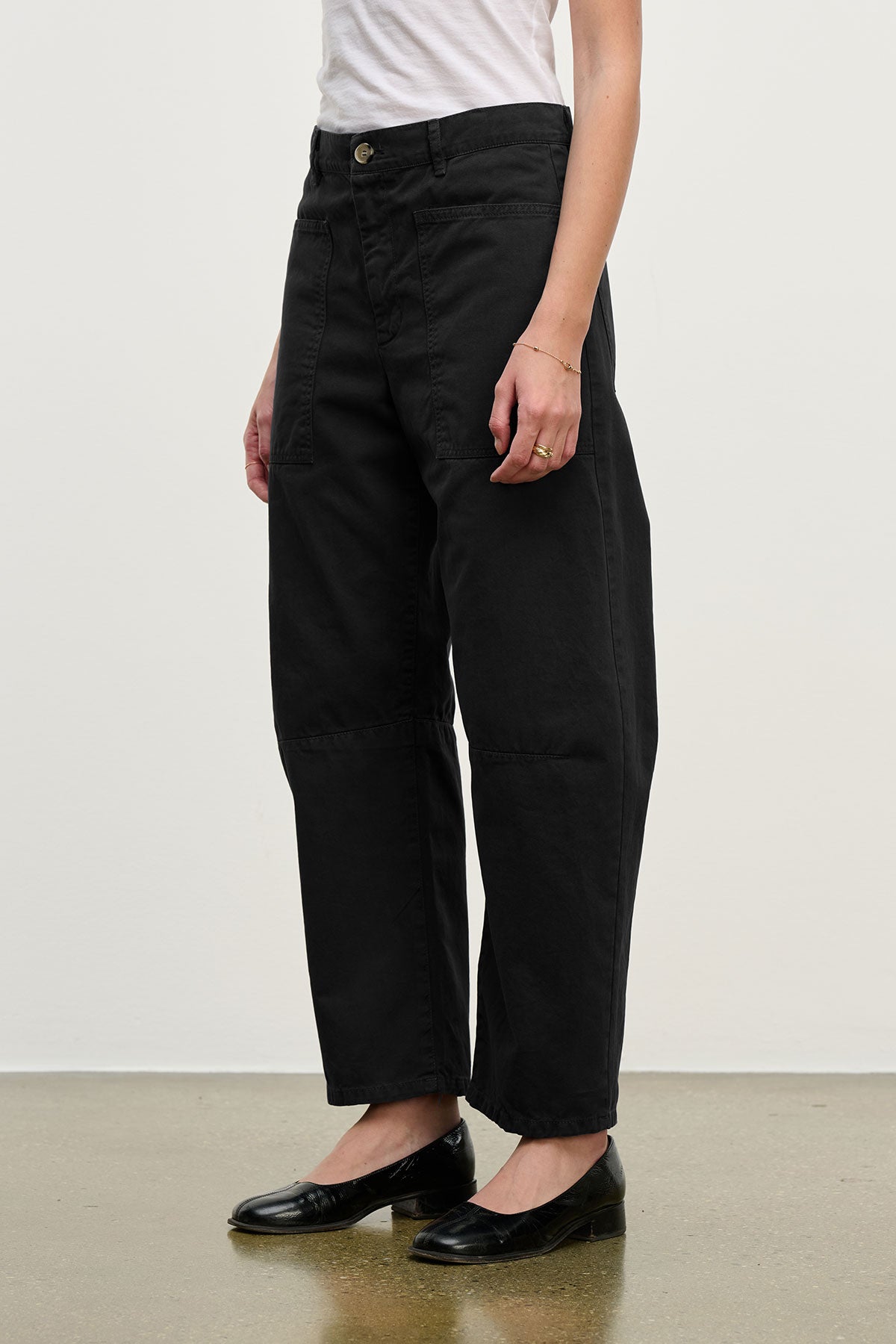 A person stands against a plain background wearing Velvet by Graham & Spencer’s BRYLIE SANDED TWILL UTILITY PANT in black, styled with a white shirt and black flats.-40416889700545