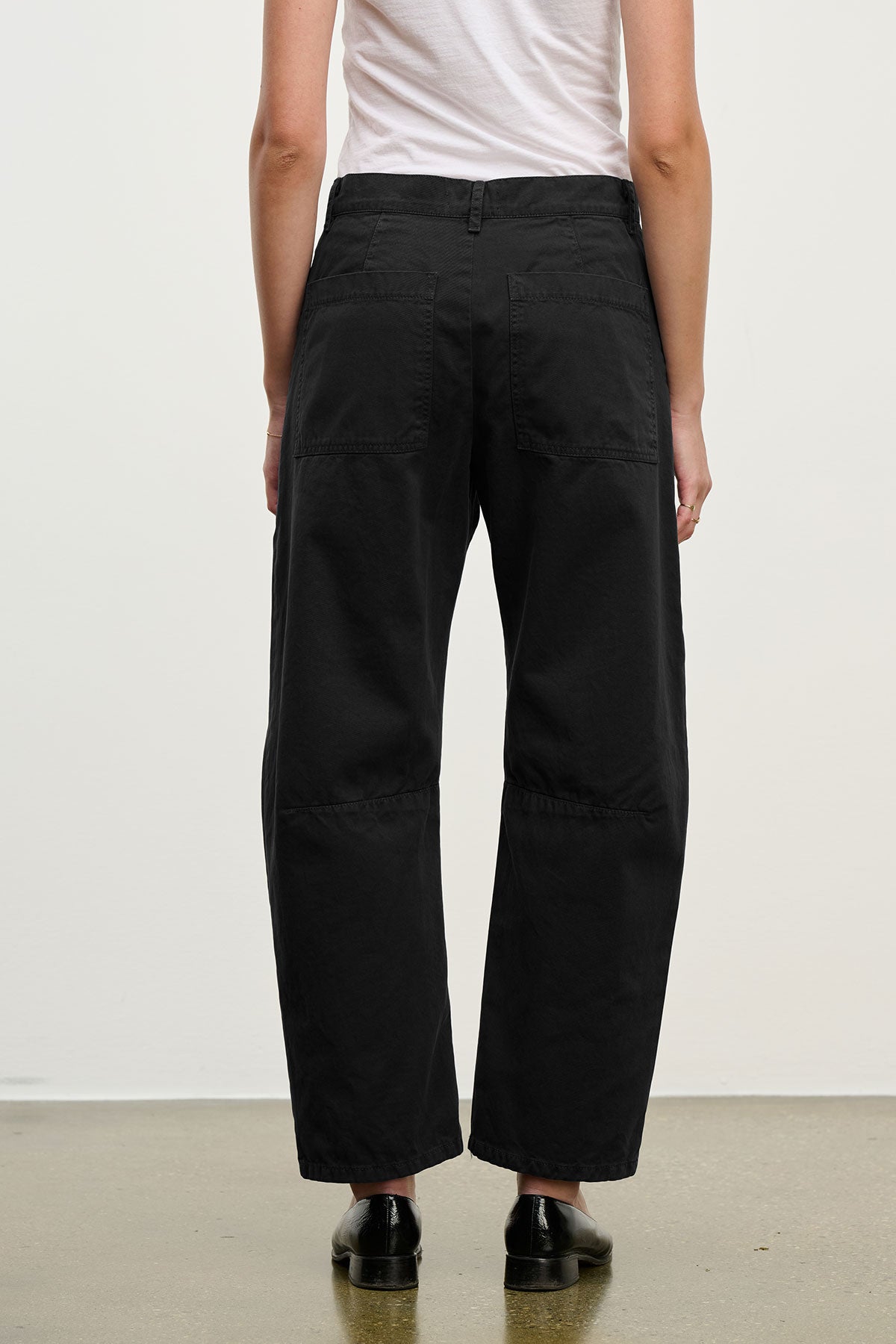 A person in a white shirt and Velvet by Graham & Spencer's BRYLIE SANDED TWILL UTILITY PANT with patch pockets stands facing away from the camera on a light-colored floor.