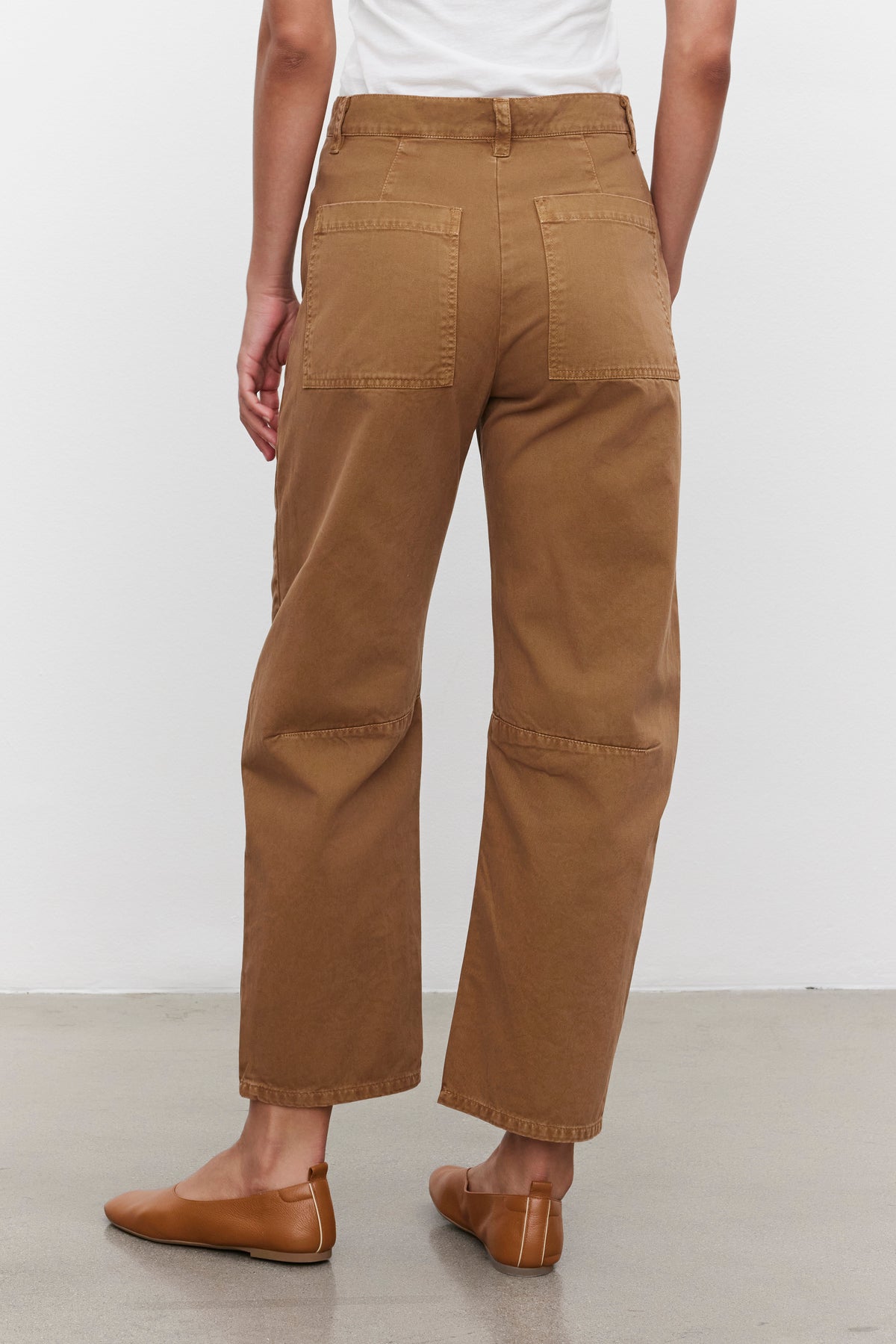   A person wearing the BRYLIE SANDED TWILL UTILITY PANT by Velvet by Graham & Spencer, which features large patch pockets, along with a white top, is seen from the back standing on a light-colored floor. 