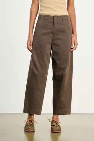 A person wearing Velvet by Graham & Spencer's DARIA PANT, a tailored wide-leg style, pairs it with a beige sleeveless top and brown moccasin-style shoes, standing against a plain background to showcase a modern silhouette.