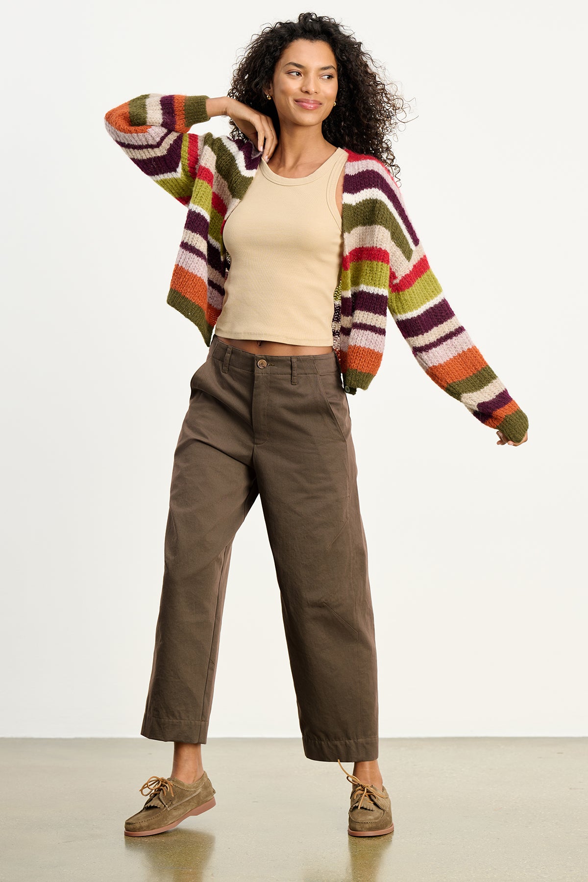 A woman models the DARIA PANT by Velvet by Graham & Spencer indoors with a striped cardigan, beige tank top, and tan shoes, highlighting its modern silhouette—a versatile essential for any wardrobe.-39789167706305