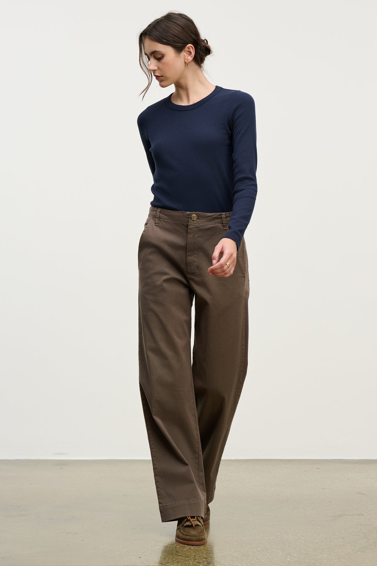 A woman stands indoors against a plain background wearing Velvet by Graham & Spencer's DEN PANT—high-waisted, cotton twill wide-leg pants with an elastic waistband—paired with a navy long-sleeve top and brown shoes.