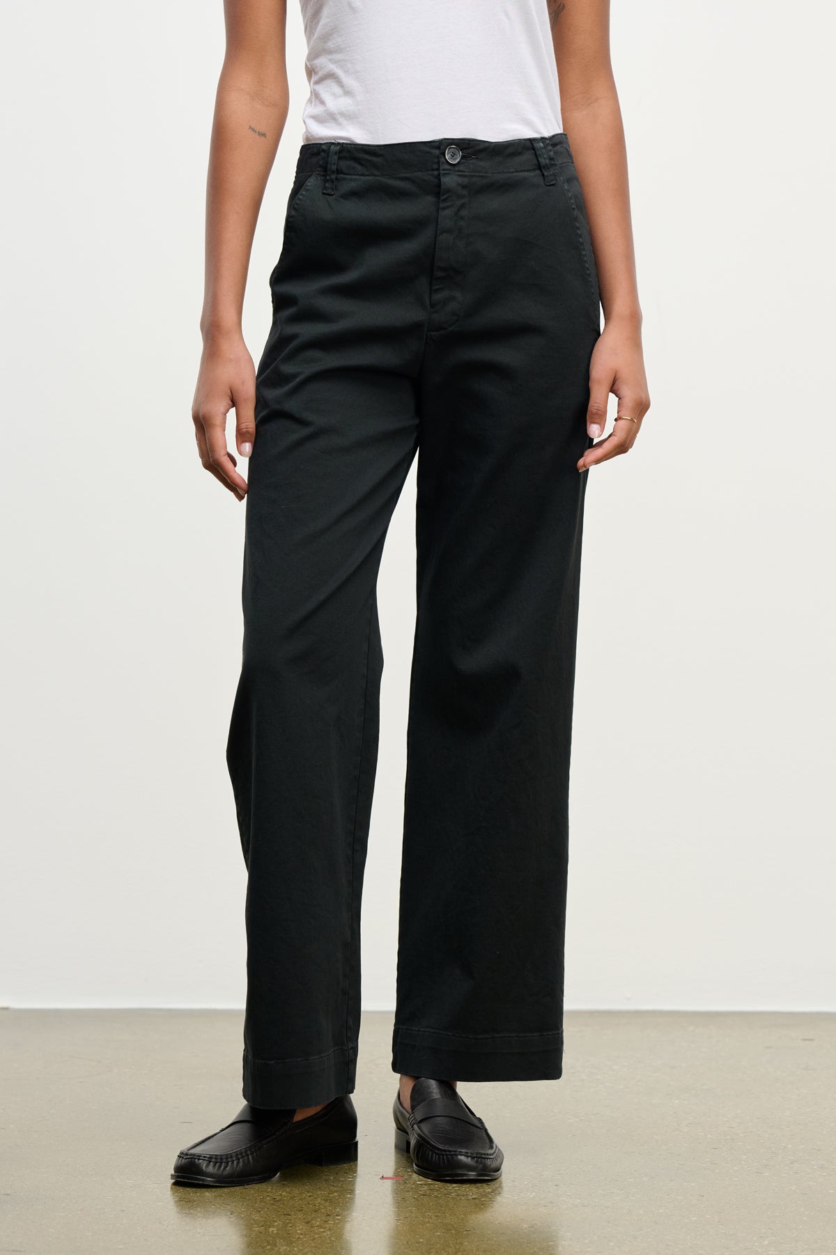 A person wearing Velvet by Graham & Spencer's DEN PANT—black wide-leg cotton twill pants with an elastic waistband—paired with a white short-sleeve shirt and black loafers stands against a plain background.