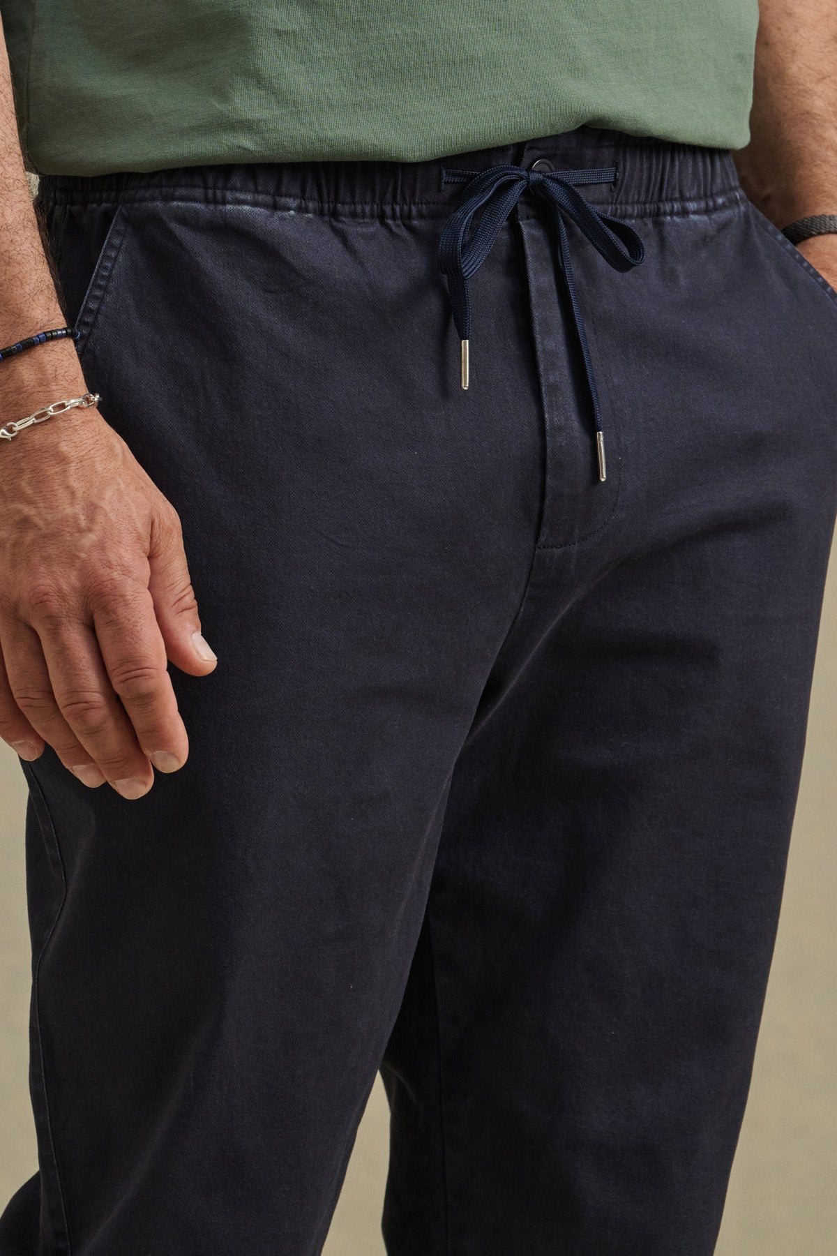 A person wearing a green shirt and the JESSE PANT by Velvet by Graham & Spencer—navy blue modern tapered pants with a tailored fit—stands with hands resting at their sides.-41009007558849