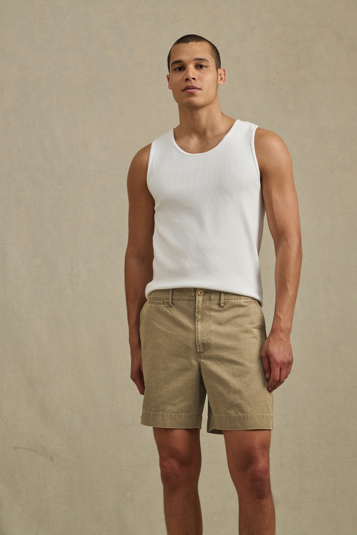 A person stands against a plain beige background, wearing a white sleeveless shirt and the JOEL SHORT by Velvet by Graham & Spencer—classic cotton twill shorts with 5-pocket styling, perfect for warm weather.