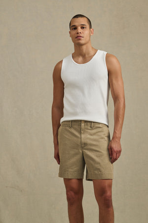 A person stands against a plain beige background, wearing a white sleeveless shirt and the JOEL SHORT by Velvet by Graham & Spencer—classic cotton twill shorts with 5-pocket styling, perfect for warm weather.