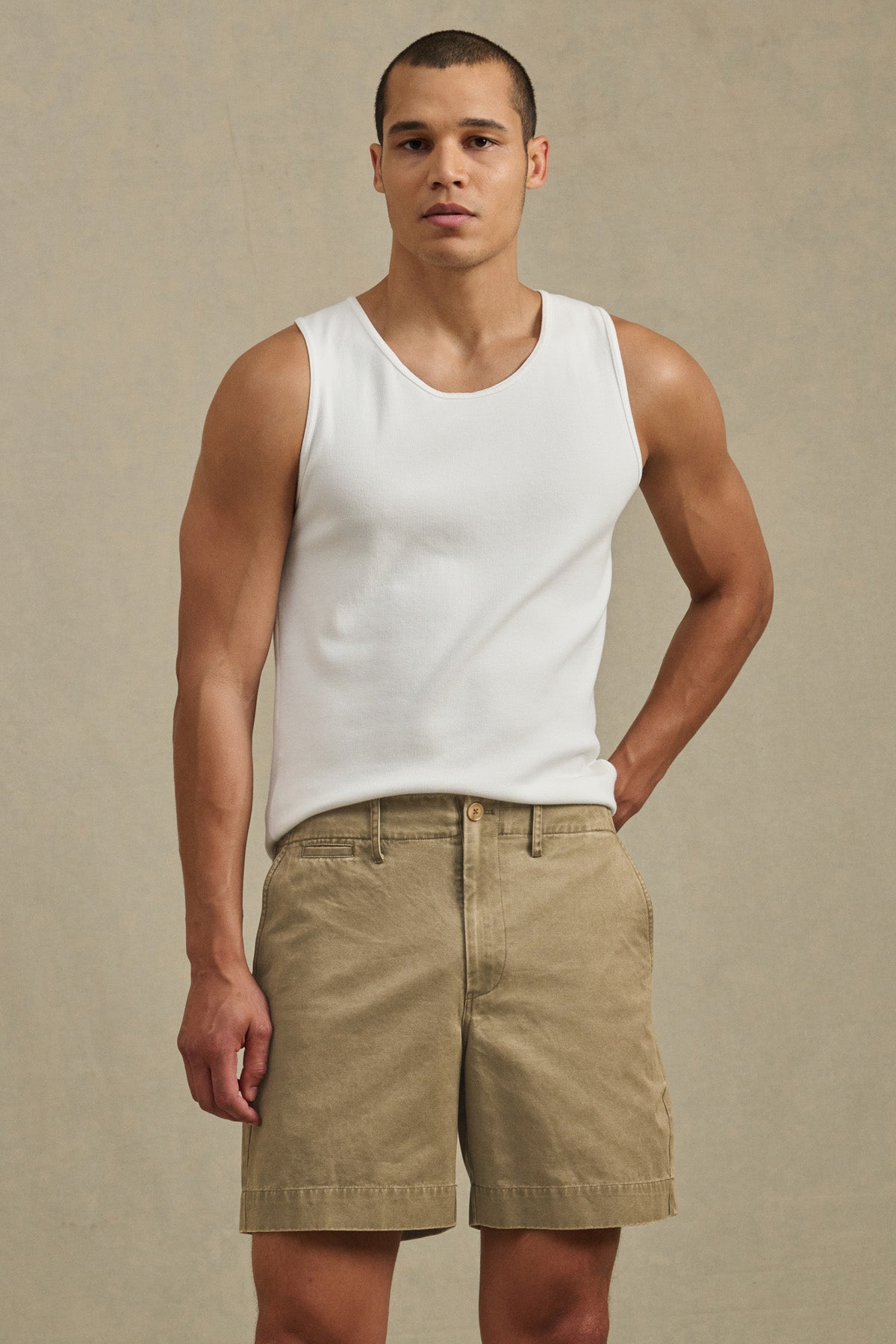 A man wearing a white sleeveless shirt and the JOEL SHORT by Velvet by Graham & Spencer, a classic 5-pocket cotton twill short, stands facing the camera against a plain beige background.