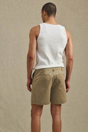 A man faces away, wearing a white tank top and Velvet by Graham & Spencer's JOEL SHORT—khaki cotton twill shorts with classic 5-pocket styling, set against a plain beige background.