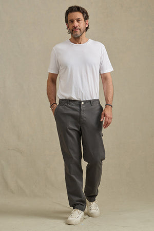 A man stands against a plain background wearing a white t-shirt and the LENNOX PANT by Velvet by Graham & Spencer in relaxed fit gray cotton twill, paired with white sneakers—an ideal look for everyday wear.
