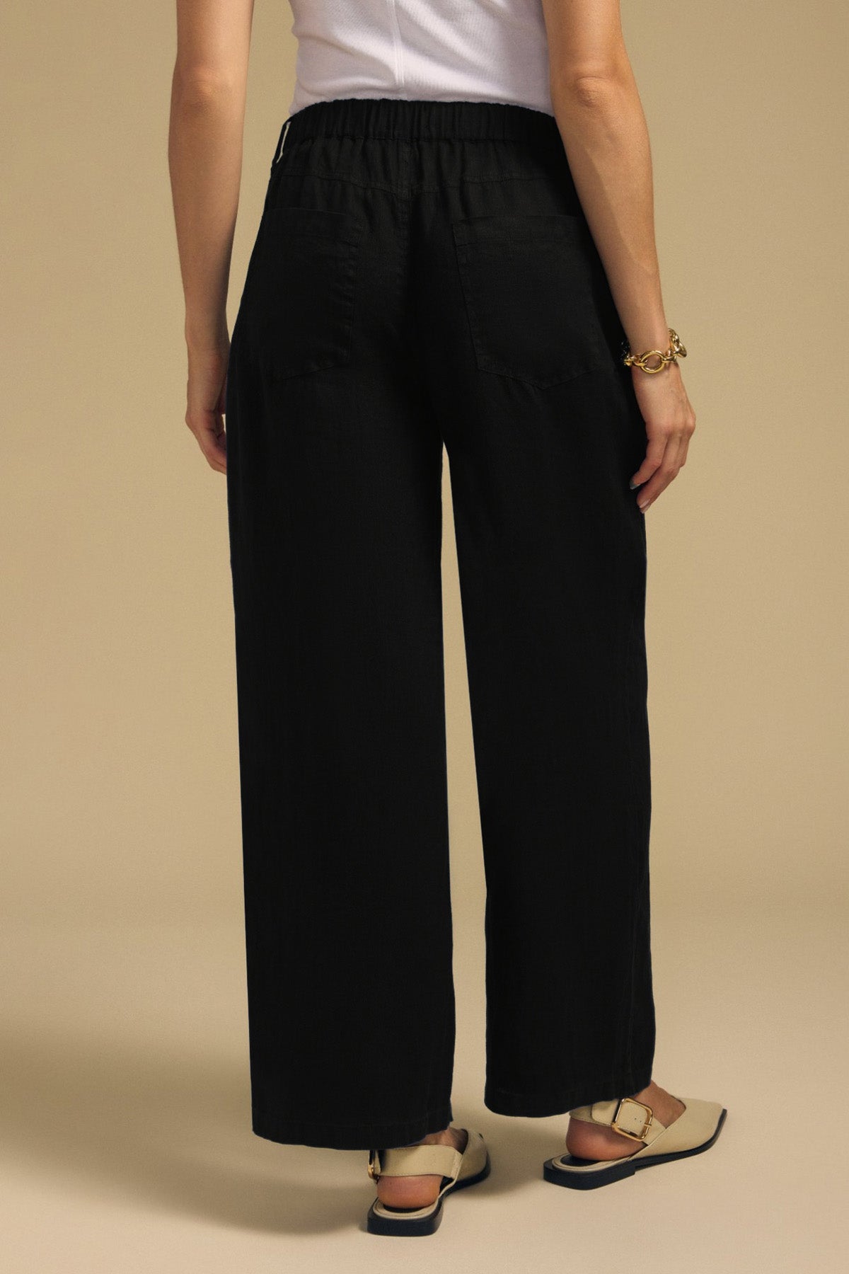A person viewed from the back wearing the PENELOPE LINEN PANT, designed with cropped, wide-leg linen trousers and an elasticized waistband.-46422298001601