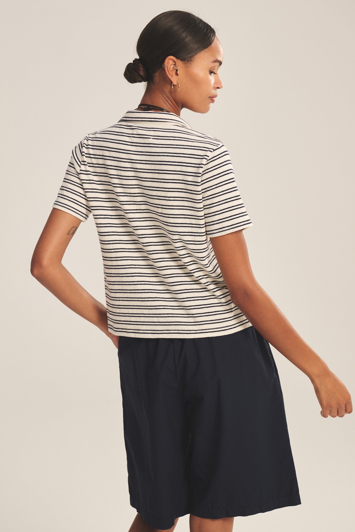 A person stands with their back turned, wearing the Velvet by Graham & Spencer PERRIN POLO in black and white stripes and navy shorts against a neutral background.-41089062961345