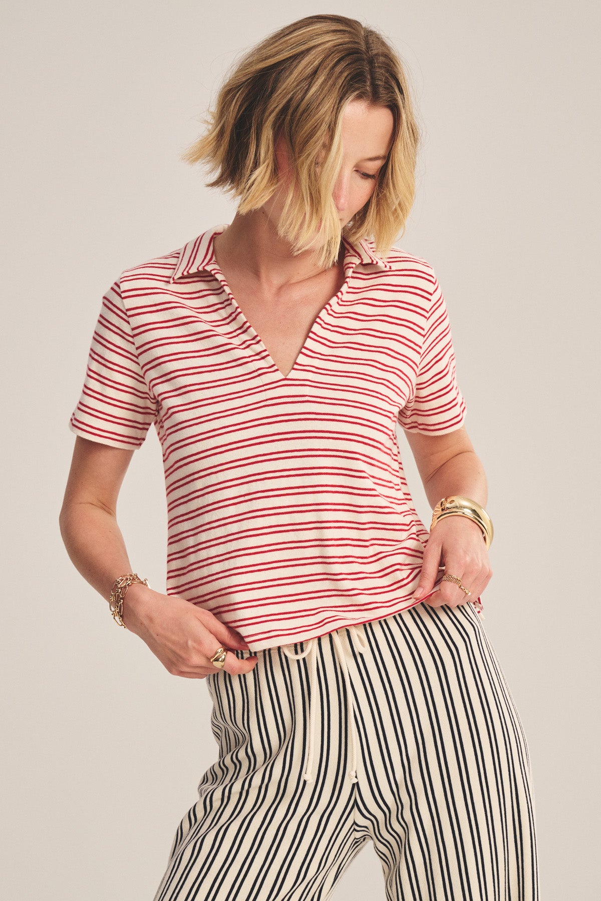 A woman models the PERRIN POLO by Velvet by Graham & Spencer, a yarn-dyed striped collared short-sleeve top, paired with high-waisted white pants with black vertical stripes, against a neutral background.-41089062895809