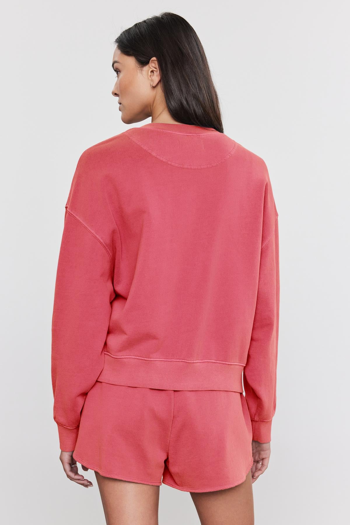 Rear view of a woman wearing a coral pink, pigment-dyed Velvet by Graham & Spencer Skylar sweatshirt and matching shorts, standing against a plain background.-36910094581953