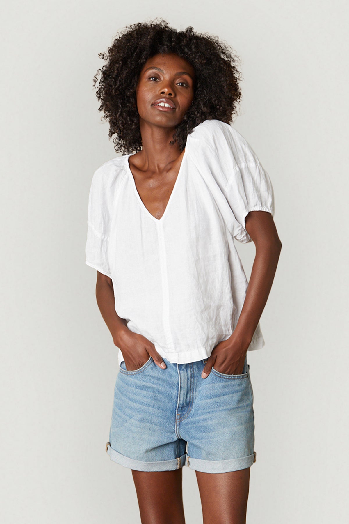   A woman standing with her hands in her pockets wearing the CALLIN PUFF SLEEVE LINEN TOP by Velvet by Graham & Spencer. 