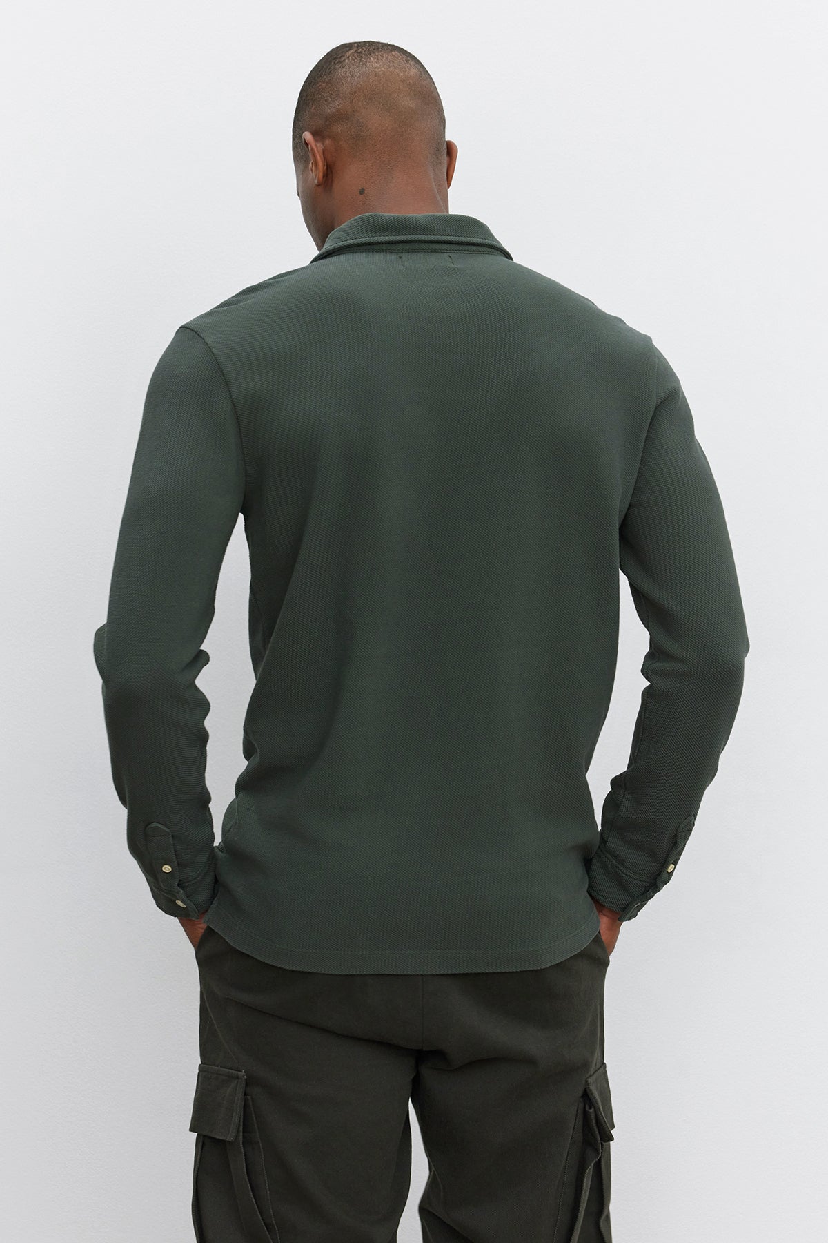   A person is shown from the back, wearing the MIKE POLO by Velvet by Graham & Spencer, a dark green long-sleeve polo made of piqué cotton, paired with matching dark green pants. 