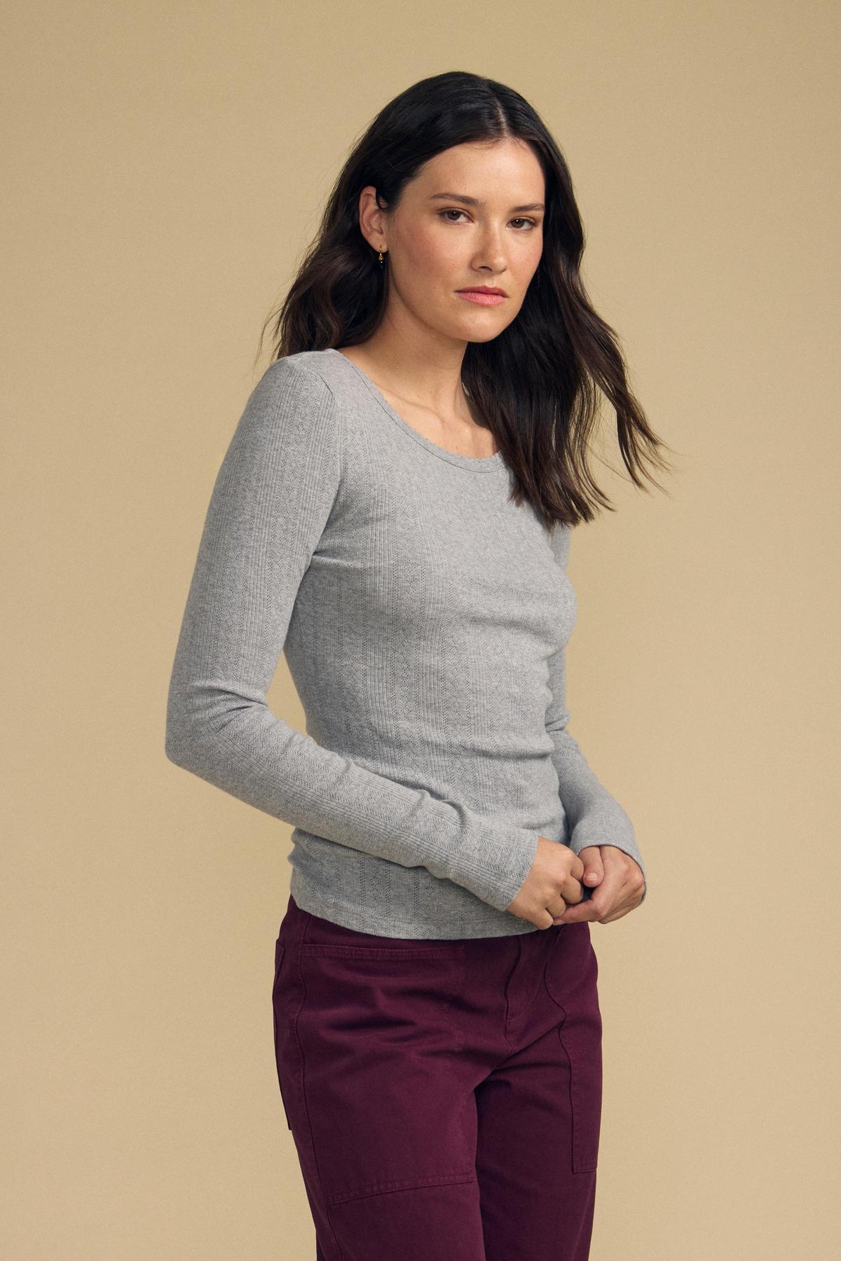 Front view of MIRIAM POINTELLE RIBBED SCOOP NECK TEE showcasing its gray long sleeves with a model against a beige background-41976351621313