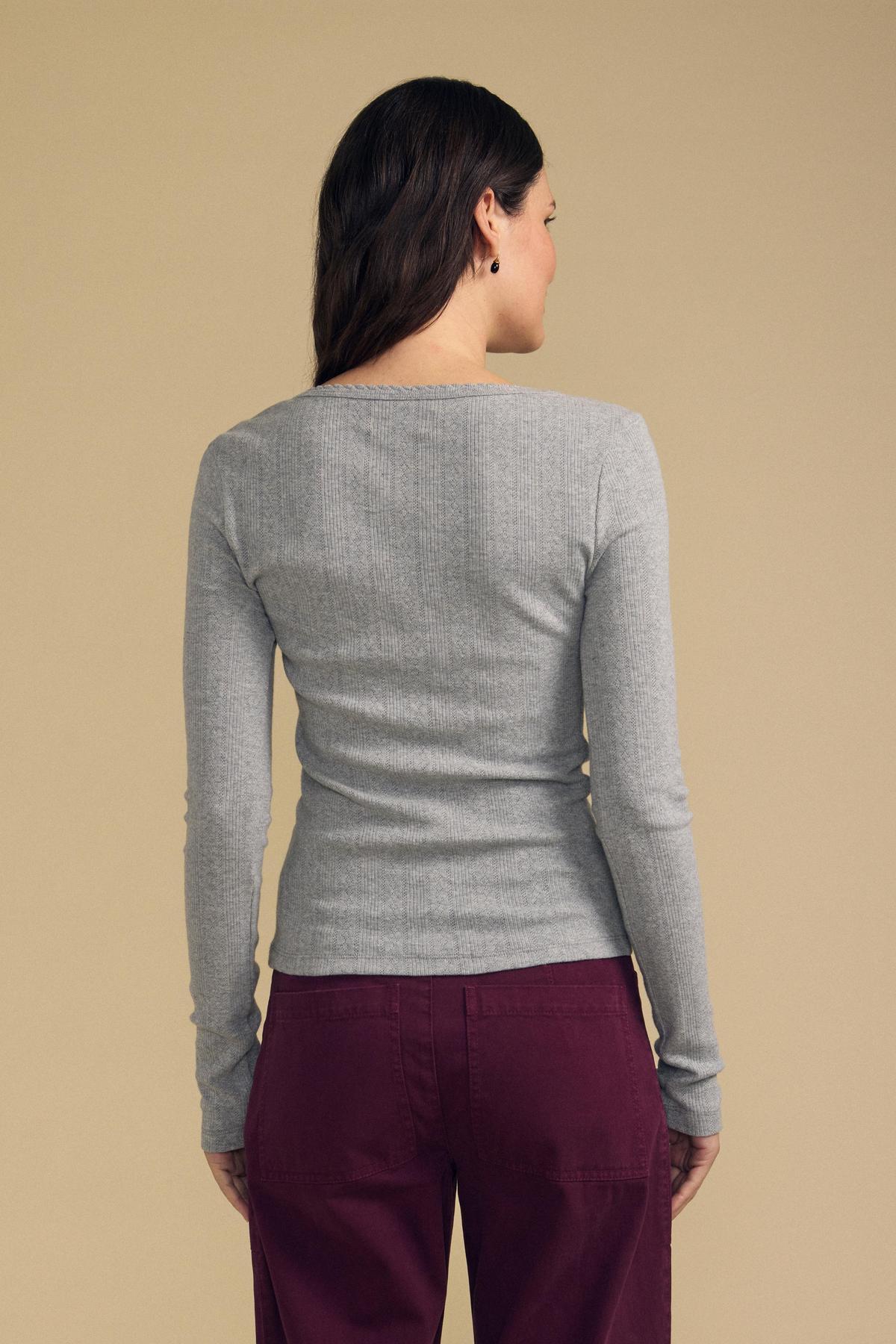 Back view of MIRIAM POINTELLE RIBBED SCOOP NECK TEE showing a fitted gray ribbed knit with long sleeves against beige