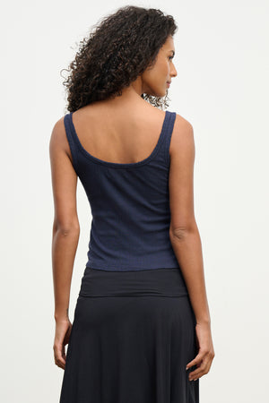 A woman with curly hair is shown from behind, wearing the ADELLE TANK TOP by Velvet by Graham & Spencer in navy blue and a black skirt against a plain light background.