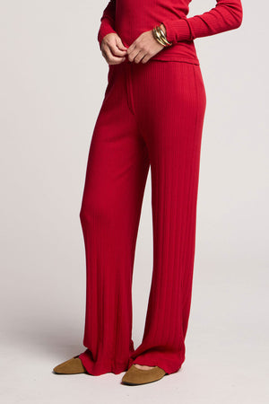 Someone wearing Velvet by Graham & Spencer's ALEMI POINTELLE PANT in red with a matching long-sleeve top, brown pointed-toe flats, and a gold bracelet, standing against a plain background.