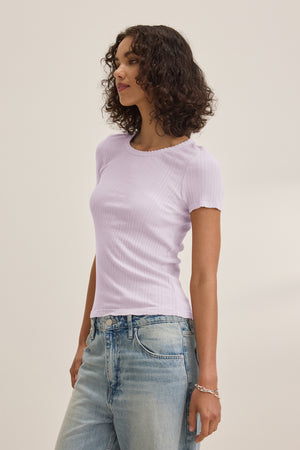 A woman wears the ENATI POINTELLE TEE by Velvet by Graham & Spencer—a light purple ribbed fitted top in a soft cotton-modal blend—paired with light blue jeans, standing against a plain light background.